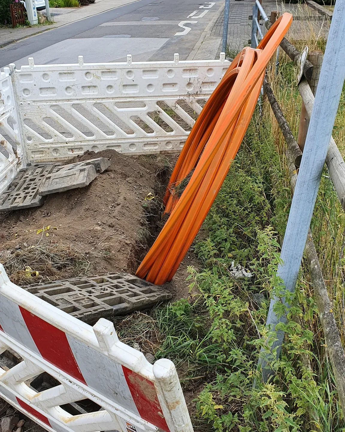 Blick auf eine Krefelder Glasfaserbaustelle mit Graben und orangefarbenen Rohren.
